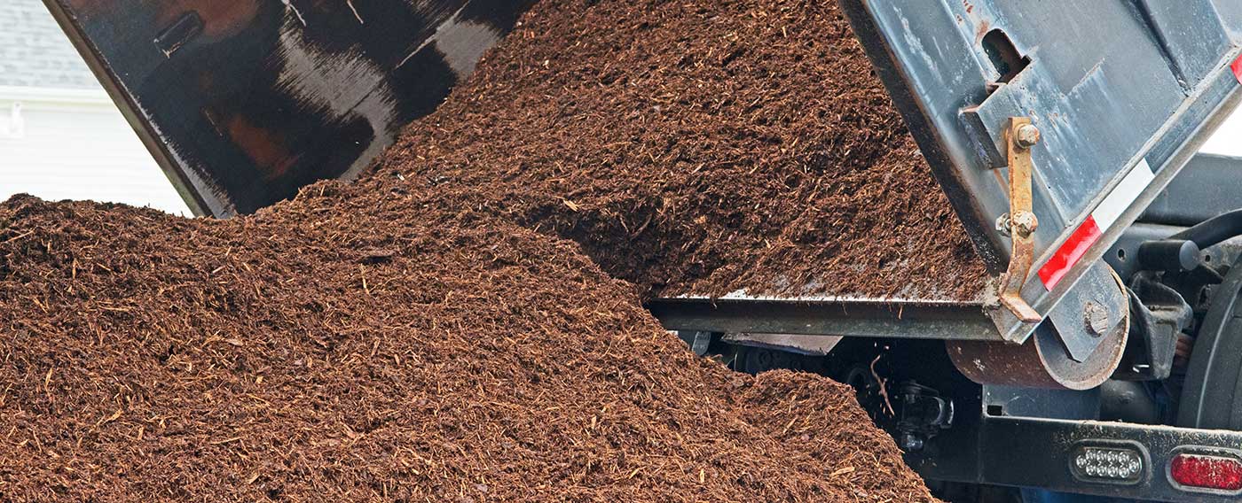 cropped photo of the back of a dump truck unloading a pile of mulch